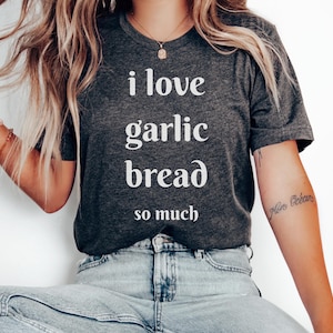 May include: Dark gray t-shirt with the text "I love garlic bread so much" in white. The shirt is made of a soft material and is suitable for casual wear. The shirt is paired with blue jeans.