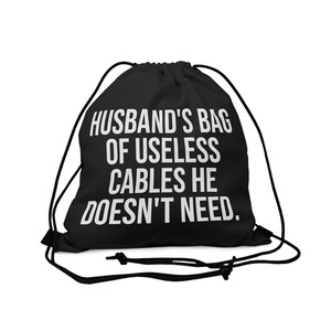 Peut inclure: Sac à cordon noir avec du texte blanc qui dit "Husband's Bag of Useless Cables He Doesn't Need."