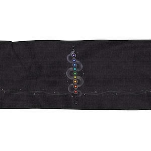 May include: A rectangular black throw blanket featuring a central graphic of a coiled snake with seven coloured circular chakra symbols along its body. A thin horizontal line with small moon and star icons extends across the centre, with fringed edges.