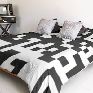 May include: A white and black geometric patterned duvet cover on a bed with a wooden frame. The duvet cover has a modern, abstract design.