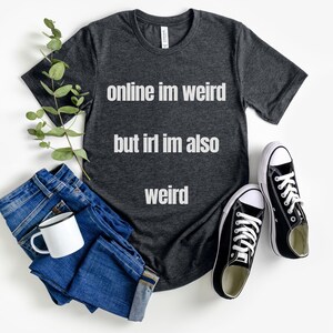 May include: A dark gray t-shirt with the text "online im weird but irl im also weird" printed in white.