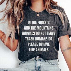 May include: A dark gray t-shirt with white text that reads "In the forests and the mountains animals do not leave trash humans do. Please behave like animals."