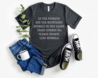 May include: A dark grey t-shirt with the text "IN THE FORESTS AND THE MOUNTAINS ANIMALS DO NOT LEAVE TRASH HUMANS DO. PLEASE BEHAVE LIKE ANIMALS." printed in white.