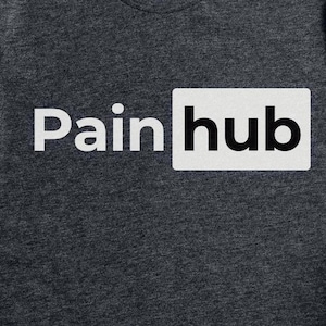 以下が含まれることがあります： 「Pain hub」の白文字が入った濃いグレーのTシャツ。「Pain」の文字はサンセリフ体で、「hub」は有名なロゴを模倣した白い長方形の中にあります。このシャツは柔らかい素材で作られています。