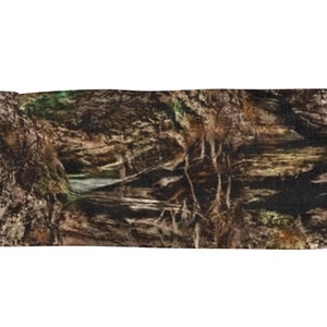 May include: A camouflage patterned fabric with a brown, green, and black color scheme. The fabric has a woven texture and a fringed edge.