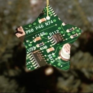 Op de afbeelding: Een groene stervormige ornament met een printplaatontwerp. De printplaat heeft verschillende componenten, waaronder weerstanden, condensatoren en geïntegreerde schakelingen. De tekst "PRO P46 N74" is zichtbaar op de printplaat.