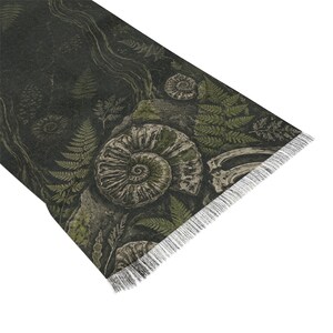 May include: A rectangular textile runner featuring a dark forest green background with a detailed print of fossilised ammonites, prehistoric fern leaves, and skeletal remains. The fabric has a textured appearance and a fringe along the edge.