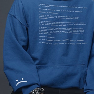 Op de afbeelding: Een blauwe hoodie met een witte tekstprint die luidt: "Er is een probleem gedetecteerd en Windows is afgesloten om schade aan uw computer te voorkomen. Het probleem lijkt te worden veroorzaakt door het volgende bestand: PROP46N74.SYS PAGE_FAULT_IN_NONPAGED_AREA Als dit de eerste keer is dat u dit stopfout-scherm ziet, start u uw computer opnieuw op. Als dit scherm opnieuw verschijnt, volg dan deze stappen: Controleer of alle nieuwe hardware of software correct is geïnstalleerd. Als het een nieuwe installatie betreft, neem dan contact op met de fabrikant van uw hardware of software voor eventuele Windows-updates die u mogelijk nodig heeft. Als de problemen aanhouden, schakel dan alle nieuw geïnstalleerde hardware of software uit of verwijder deze. Schakel BIOS-geheugenopties zoals caching of shadowing uit. Als u de veilige modus moet gebruiken om onderdelen te verwijderen of uit te schakelen, start u uw computer opnieuw op, druk op F8 om de geavanceerde opstartopties te selecteren en selecteer vervolgens de veilige modus. Technische informatie: *** STOP: 0x00000050 (0xD1094C2, 0x00000001, 0x874F7617, 0x00000000) *** 8841w45H. ON17 - Adres FF7617 basis op 5000, tijdstempel 1dd6dc7c"