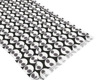 May include: Black and white scarf with a repeating pattern of stylized eyes. The scarf has a fringed edge.