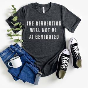 May include: A dark grey t-shirt with the text "THE REVOLUTION WILL NOT BE AI GENERATED" printed in white.