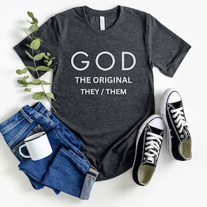 Puede incluir: Una camiseta gris oscuro con el texto "GOD THE ORIGINAL THEY/THEM" impreso en blanco.