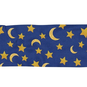 Pode incluir: Têxtil retangular azul com um padrão repetido de estrelas douradas e luas crescentes. As bordas têm franjas. Pode ser um lenço, um cobertor ou um elemento decorativo.