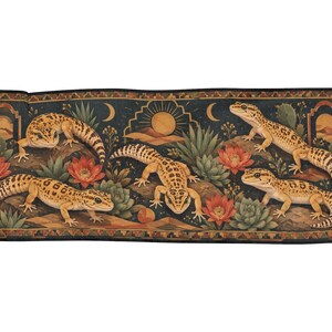 Könnte beinhalten: Ein rechteckiger Webteppich mit vier Leopardgeckos in einer Wüstenlandschaft mit Kakteen, Sukkulenten und roten Blüten. Der dunkle Hintergrund zeigt ein Sonnen- und Mondmotiv, eingerahmt von einer geometrischen Bordüre mit Fransen an den Seiten.
