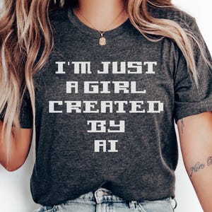 May include: A gray t-shirt with the text "I'm just a girl created by AI" printed in white.