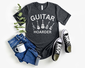 May include: A dark gray t-shirt with the text "GUITAR HOARDER" in white. The shirt features a graphic of five different guitars.