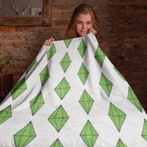 May include: White blanket featuring a repeating pattern of green diamond shapes. The diamonds have a three-dimensional appearance with black outlines. The blanket is displayed against a brick wall background.