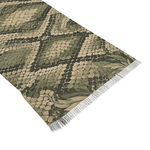 Puede incluir: Una alfombra rectangular tipo pasillero con un patrón de diamantes repetido en tonos verde oliva, beige y negro, que imita la textura de piel de serpiente. La alfombra tiene flecos blancos cortos y finos en el borde inferior.