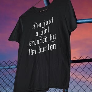 May include: Black t-shirt with white text in a gothic font that reads "I'm just a girl created by Tim Burton".
