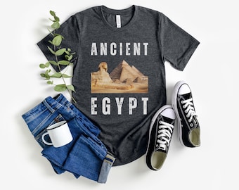 Puede incluir: Una camiseta gris oscuro jaspeada con un gráfico de estilo vintage de la Gran Esfinge y las Pirámides de Giza. El texto "ANCIENT EGYPT" está impreso en blanco en la camiseta.