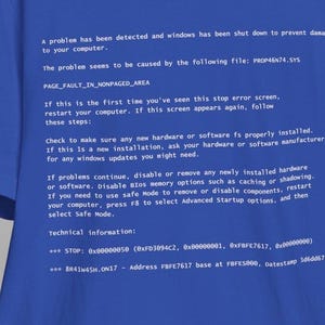 Puede incluir: Camiseta azul con texto blanco que muestra un mensaje de error de Windows, incluyendo instrucciones e información técnica. El diseño recuerda la 'Pantalla Azul de la Muerte'. Un artículo humorístico para entusiastas de la tecnología.