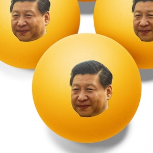 May include: Four yellow ping pong balls with a portrait of the same man on each ball.