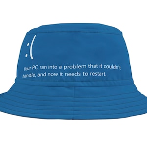 Pode incluir: Um chapéu de pescador azul com o texto "Your PC ran into a problem that it couldn't handle, and now it needs to restart." e um emoji de rosto triste.