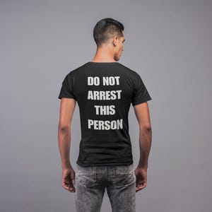 May include: A black t-shirt with the text "DO NOT ARREST THIS PERSON" printed on the back in white.