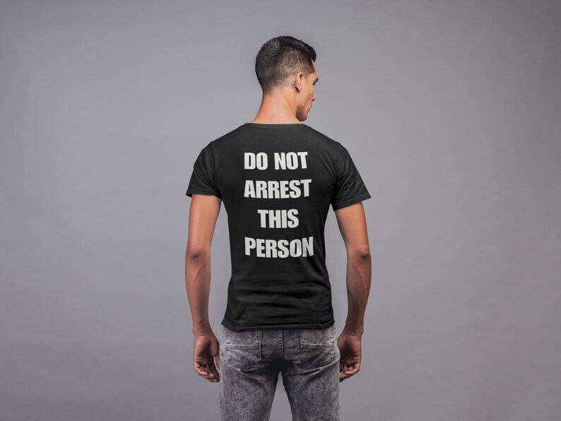 May include: A black t-shirt with the text "DO NOT ARREST THIS PERSON" printed on the back in white.