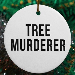 May include: White round ceramic Christmas ornament with black text that reads "TREE MURDERER".
