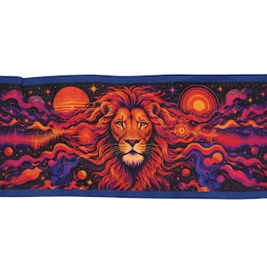 Puede incluir: Un tapiz rectangular tejido que presenta una cabeza de león central con una melena fluida en tonos naranja, rojo y morado. El fondo representa una escena cósmica con planetas, estrellas y nubes de nebulosa onduladas en tonos vibrantes.
