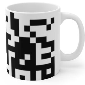 Puede incluir: Taza de cerámica blanca con un diseño pixelado en blanco y negro.