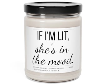 May include: A white candle jar with a black lid and a label that reads "IF I'M LIT, she's in the mood." The label also includes the text "100% NATURAL VEGAN SOY WAX ECO-FRIENDLY NON-TOXIC III MADE IN USA • REUSABLE GLASS JAR • BE THE SPARK III"