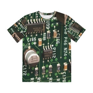 May include: A short-sleeved t-shirt featuring a detailed print of a green circuit board. The design includes various electronic components, text, and numbers, creating a tech-inspired aesthetic. The shirt is a unique blend of technology and fashion.