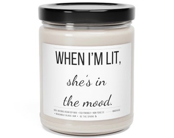 May include: A white candle jar with a black lid and a white label that reads "WHEN I'M LIT, she's in the mood." The label also includes the text "100% NATURAL VEGAN SOY WAX - ECO-FRIENDLY - NON-TOXIC 100 - MADE IN USA - REUSABLE GLASS JAR - BE THE SPARK"
