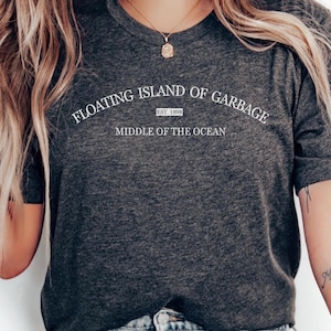 May include: A dark gray t-shirt with white text that reads "Floating Island of Garbage Est. 1998 Middle of the Ocean".