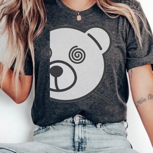 May include: A dark gray t-shirt with a white graphic of a bear's face with a spiral in its eye. The bear's face is partially obscured by the edge of the shirt.