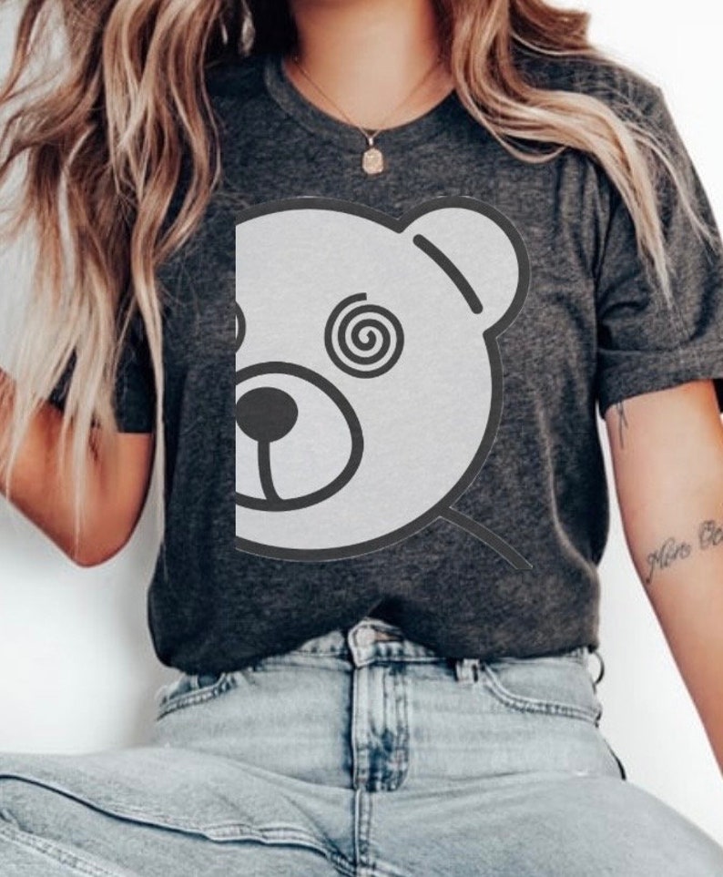 May include: A dark gray t-shirt with a white graphic of a bear's face with a spiral in its eye. The bear's face is partially obscured by the edge of the shirt.