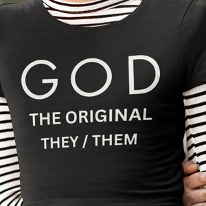 Puede incluir: Camiseta negra con texto blanco que dice "GOD THE ORIGINAL THEY/THEM"