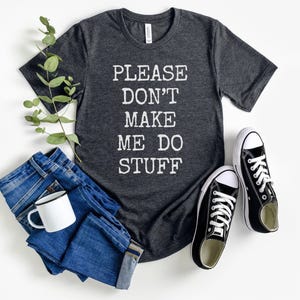 May include: A dark gray t-shirt with the text "PLEASE DON'T MAKE ME DO STUFF" printed in white.