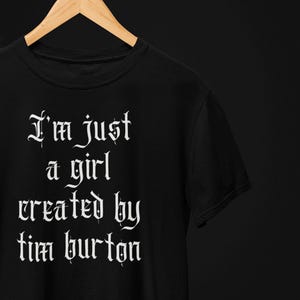 May include: Black t-shirt with white text in a gothic font that reads "I'm just a girl created by tim burton".