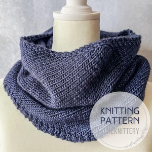 May include: A dark blue knitted cowl scarf displayed on a mannequin. The scarf has a textured, ribbed design and a rolled edge. The text "KNITTING PATTERN" and "KNITTERY" is visible on the lower right side of the image.