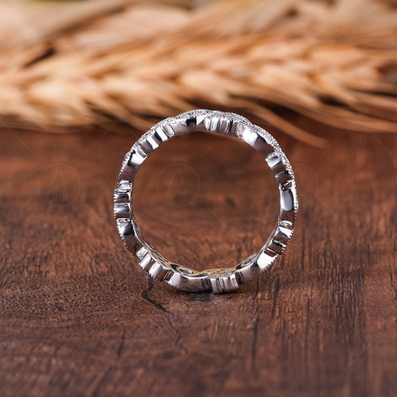 May include: A silver-toned eternity band ring featuring a continuous series of small, clear, sparkling stones set along the entire circumference of the metal band, which displays a polished finish and a scalloped, textured edge design.