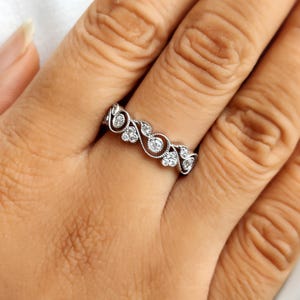 May include: A silver-toned metal ring featuring a continuous band with intricate swirling scrollwork patterns. The design is accented with small, round, clear stones embedded within the metal curves, creating a textured and detailed surface.