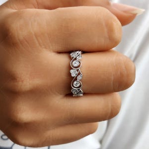 May include: A silver-toned ring featuring a delicate, intricate filigree design with swirling metal patterns and small, round, clear stones embedded throughout the band, creating a continuous, detailed texture across the surface of the jewelry.