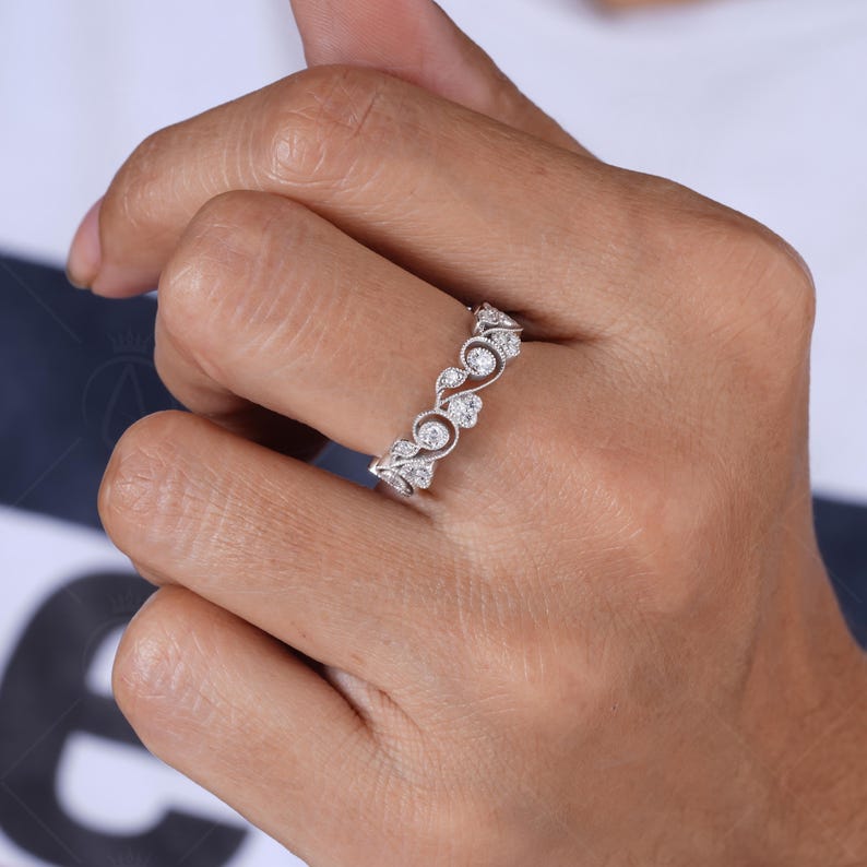 May include: A silver-toned ring featuring a delicate vine-inspired band with intricate metalwork and small, round, clear stones set along the top. The design incorporates swirling leaf-like patterns that wrap around the finger in a continuous band.