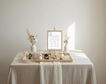 May include: A display of small objects on a wooden tray, including a microphone, figurines, and a wooden ball. A framed sign with text and illustrations is propped up on a small easel. The display is on a table with a white tablecloth, with vases of dried flowers.
