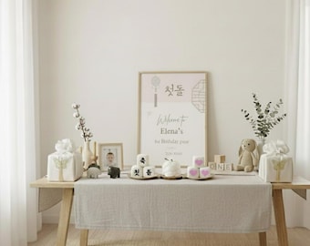 May include: A light wood table is set for a first birthday party. The table is decorated with gifts, a framed photo, small cakes, and a sign that reads "Welcome to Elena's 1st Birthday pair". A stuffed bunny and floral arrangements complete the scene.