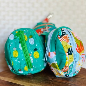 May include: Three small zippered pouches with different patterns. One pouch is green with a pineapple pattern, another is blue with a tropical leaf pattern, and the third is green with a floral pattern.