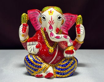 May include: A colorful hand-painted metal figurine of the Hindu deity Ganesha. The figurine is red, pink, white, blue, and yellow. Ganesha is depicted with an elephant head, a single tusk, and four arms. He is sitting with his legs crossed and holding a sweet in one hand.