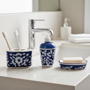 Puede incluir: Un juego de baño de cerámica azul y blanco con un soporte para cepillos de dientes con dos cepillos, un dispensador de jabón y un jabonera. El juego tiene un patrón floral y está sobre una encimera blanca.